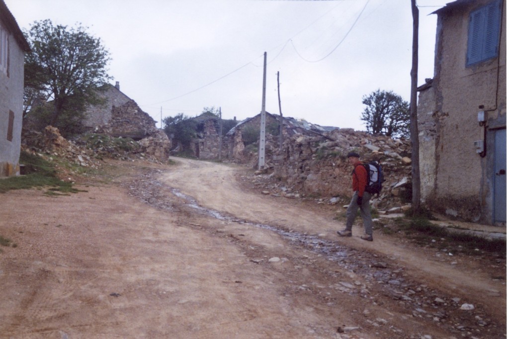 Le pèlerin dans une rue de Foncebadón, entre les maisons effondrées